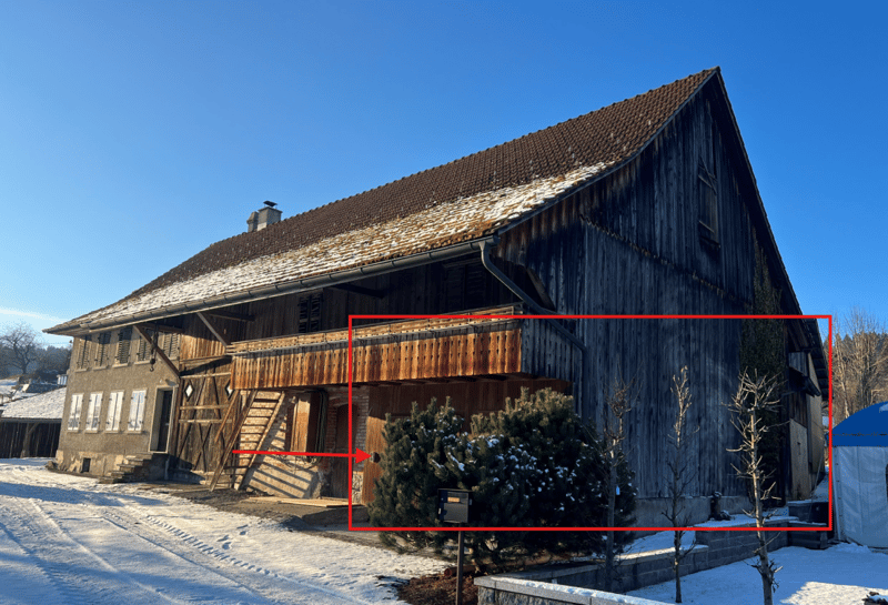 Timber-framed house with tiled roof, wooden balcony, wooden walls, entrance on the left, snow on the roof