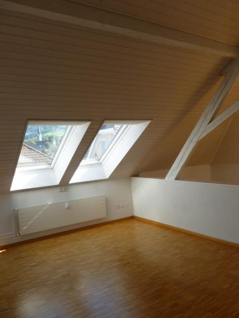 empty room with wooden floor, white walls, ceiling with wooden beams, three skylights, radiator