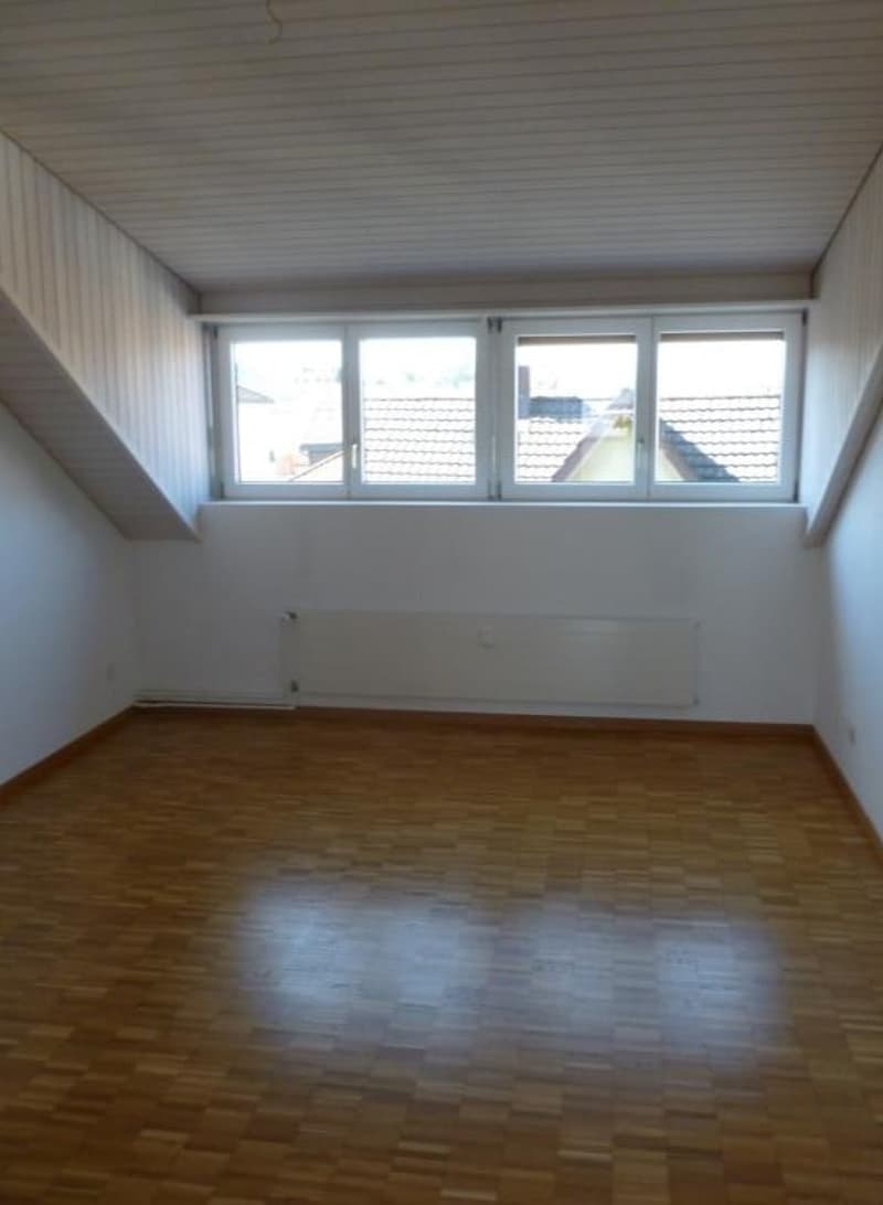 Empty room with wooden floors, white walls, and large windows.
