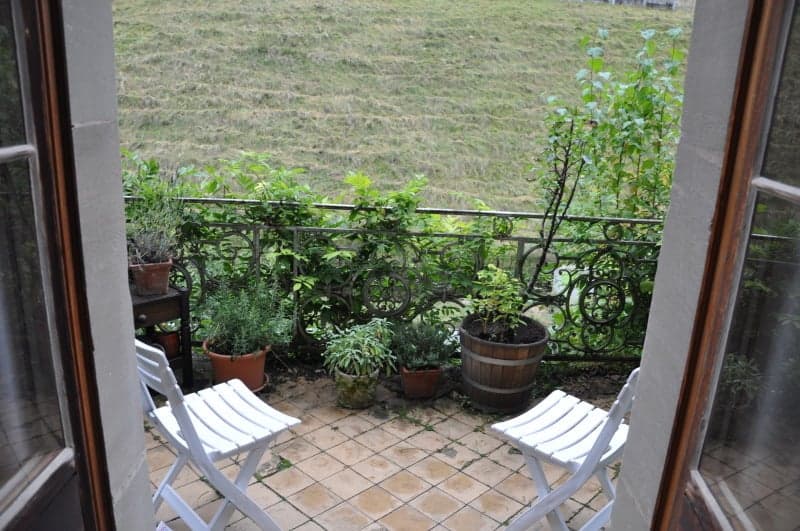 tiled floor, metal railing, several potted plants, two white chairs, overlooking a grassy field