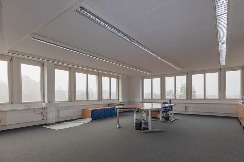 spacious office room with large windows, desks, and cabinets