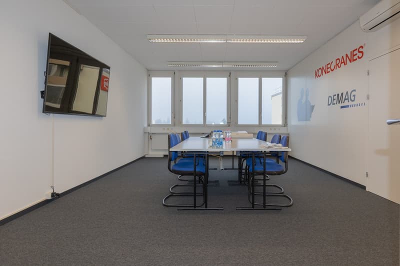 empty room, desk, chairs, flatscreen TV mounted on wall, windows, carpeted floor