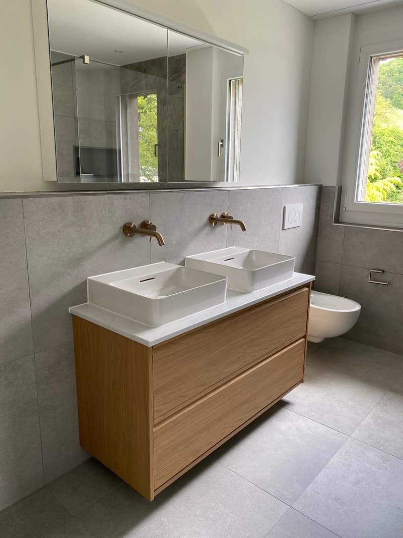 Modern bathroom with double vanity sink, wooden vanity cabinet, gray tile walls, and large mirror
