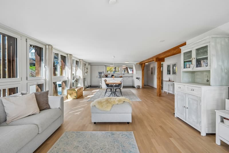 open living room with dining area, large windows, wooden floor, gray couch, white cabinets, dining table, rug