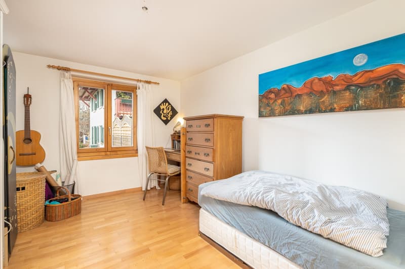 wooden floor, white walls, bed, desk, chair, storage baskets, painting on the wall, window with curtains, guitar