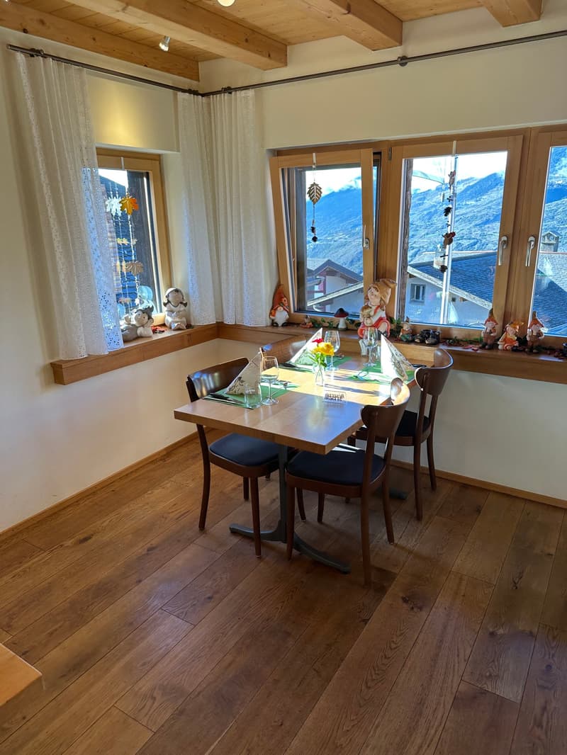 Wooden dining table with chairs, wooden ceiling beams, large windows with mountain view, decorative figurines on the windowsill