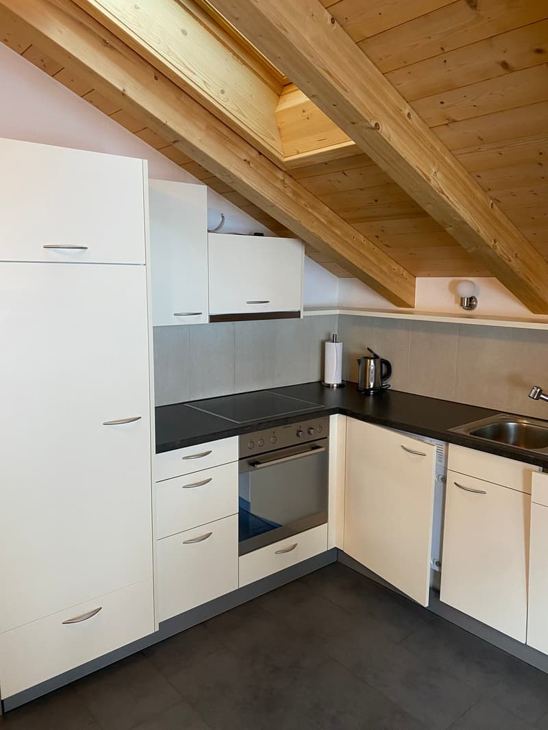 Attic kitchen with wooden beams, white cabinets, black countertops, built-in oven and dishwasher