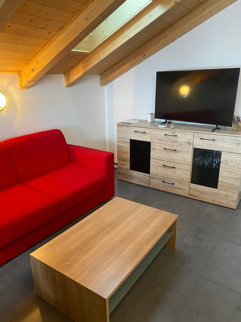 Cozy living room with a red sofa, wooden TV stand, and exposed wooden beams on the ceiling.
