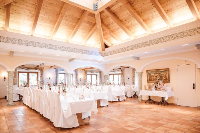 Large dining room with high wooden ceiling, ornate molding, arched windows, white tablecloths, and a fireplace