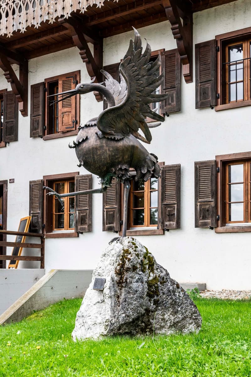 white house, wooden balcony, wooden shutters, bronze statue of a bird, grass