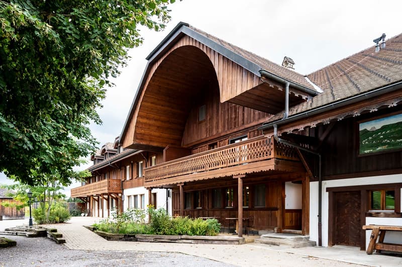 brown wooden chalet style house, large arched window, multiple windows, balcony, patio, small garden in front