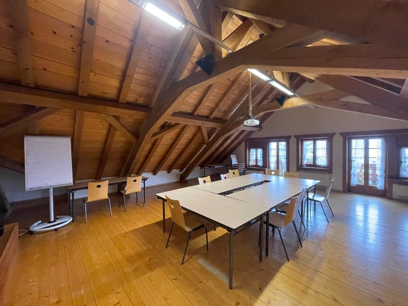 long wooden tables, wooden chairs, flip chart, three windows, wooden floors