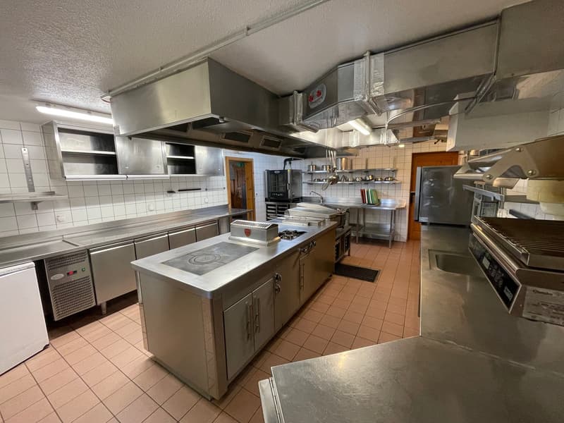 Stainless steel countertops, built-in ovens, extractor hoods, tiled floor, tiled walls, large sink, shelves, and commercial kitchen appliances.
