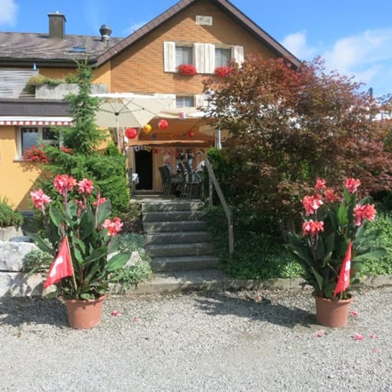 2 story house, yellow exterior, red flowers, stairs, patio, umbrella, flag