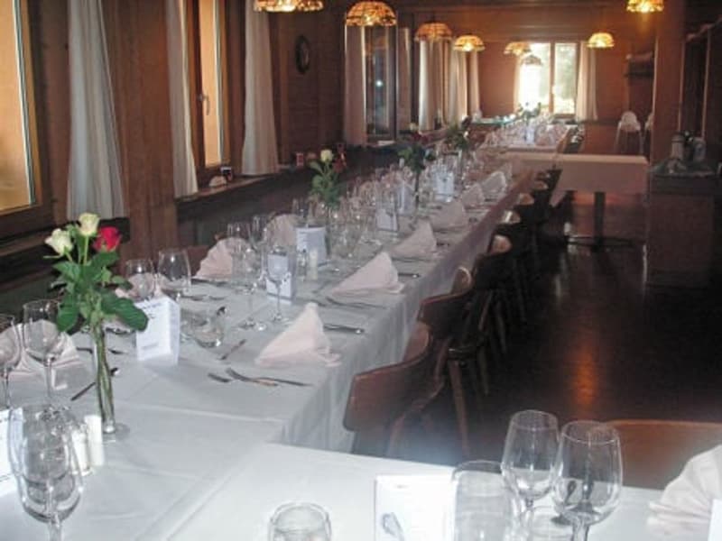 Dining room with long table, chairs, white tablecloth, wine glasses, flowers, napkins, cutlery, lamps