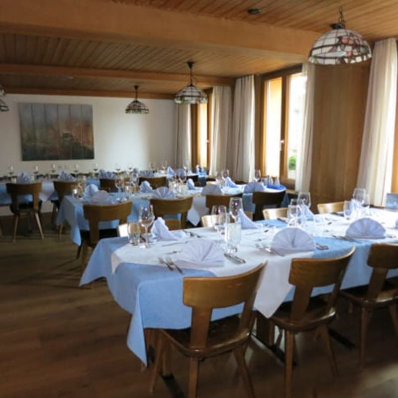 Dining room with wooden chairs, tables, blue tablecloths, wine glasses, and napkins