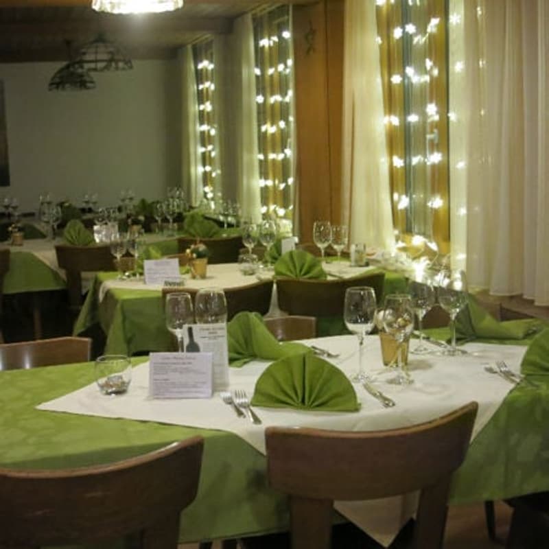 A restaurant with multiple tables and chairs, green tablecloths, wine glasses, and green napkins.
