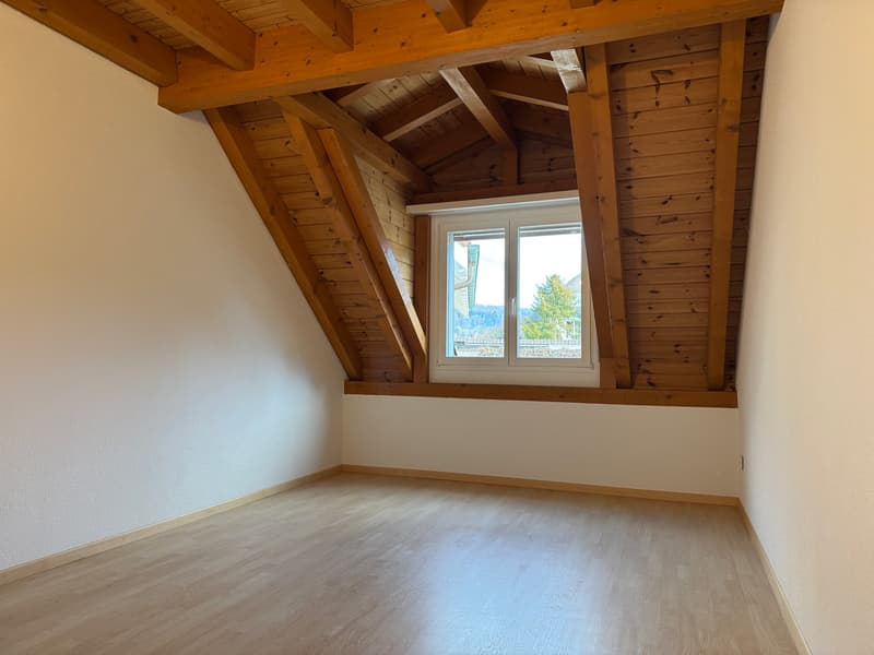 Empty attic room with wooden ceiling, wooden flooring, white walls, small attic window