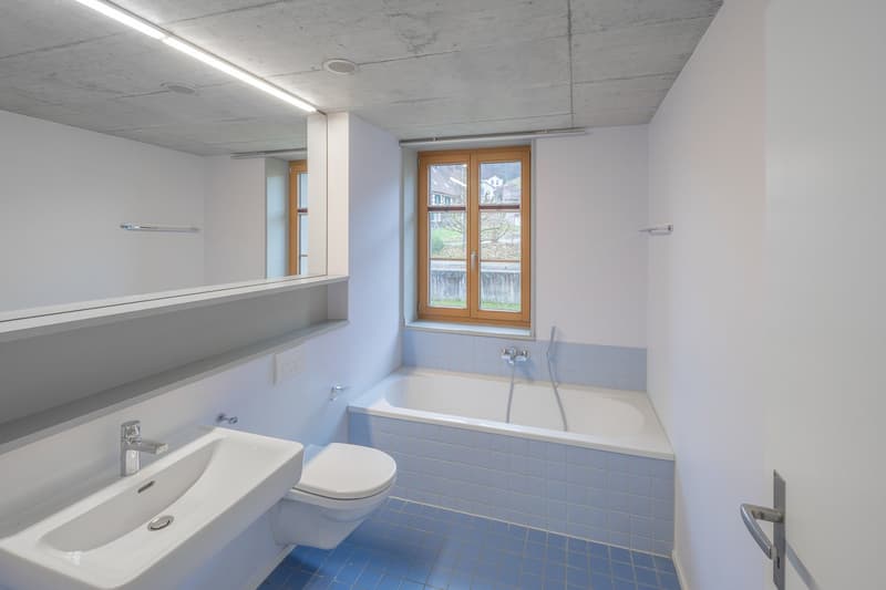 modern bathroom with a white sink, a white toilet, a blue-tiled bathtub, and a large mirror