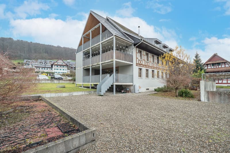 modern house, 3 stories, large balcony, metal railings, grey gravel driveway, mountain in background