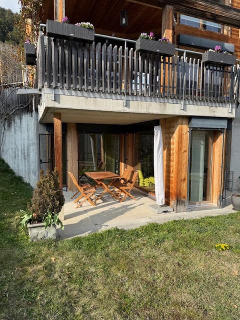 2 story house, wooden exterior, balcony with railings, outdoor dining table and chairs, potted plants