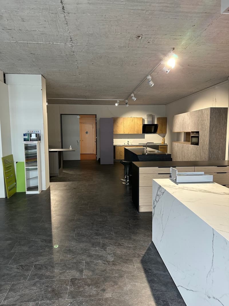 Open space with modern design, marble counter, wooden cabinets, bar stools, white shelves, kitchen area with sink, appliances, tiled floor, track lighting on ceiling