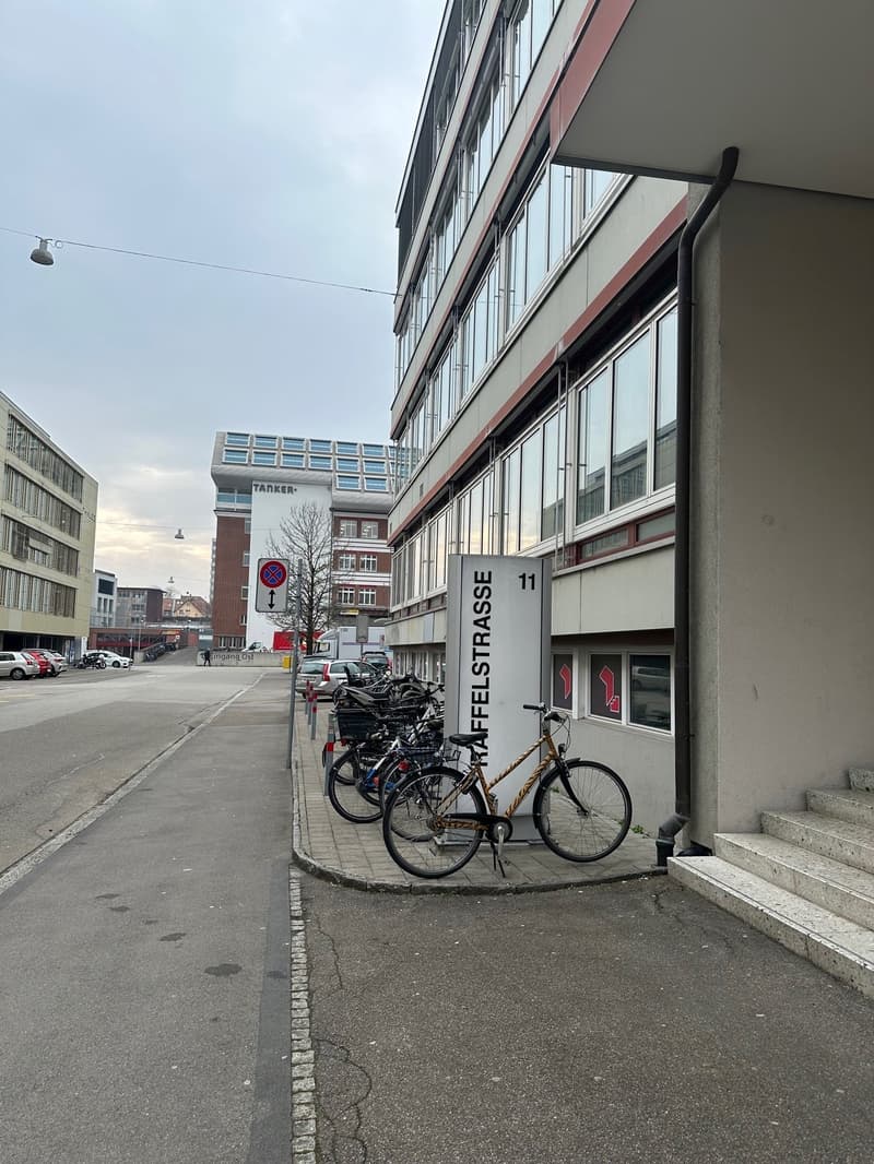 Outdoor building area, multiple bikes parked, building with large windows, and staircase leading up.