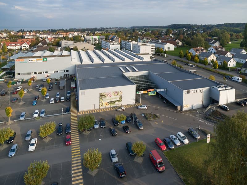 Large building, parking lot, surrounded by trees, houses in the background