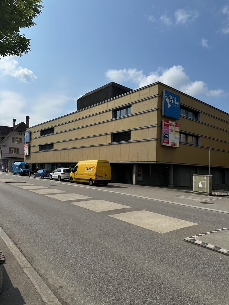 A yellow building with a blue sign that reads 'Seeland Center', several windows, and a yellow van parked in front.