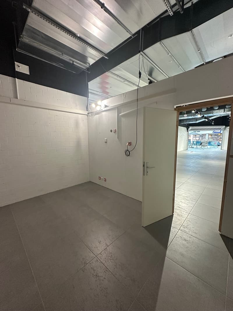Empty room with white brick wall, gray tiled floor, white door, electrical outlets, and lights on the ceiling.