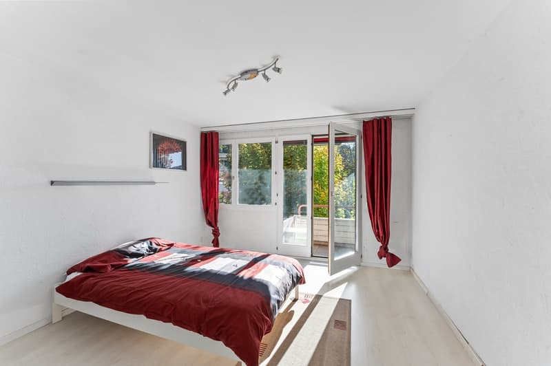 A bedroom with a double bed, white walls, hardwood floor, a glass door to the balcony, and a picture frame above the bed.