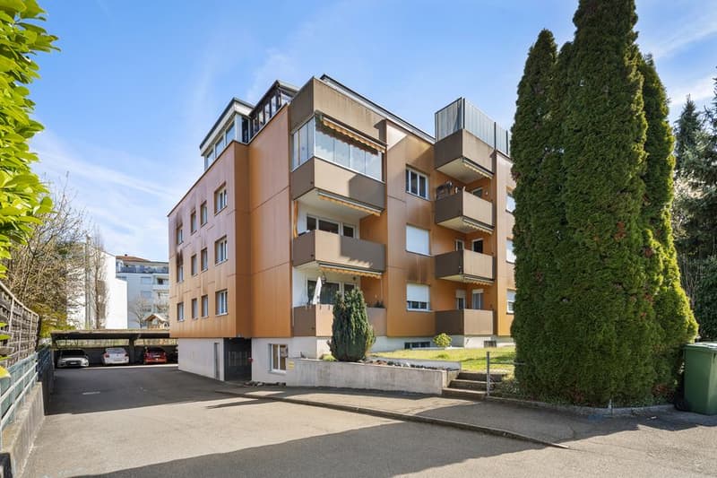 multi-story building, brown exterior, multiple balconies, underground parking, trees, and shrubs