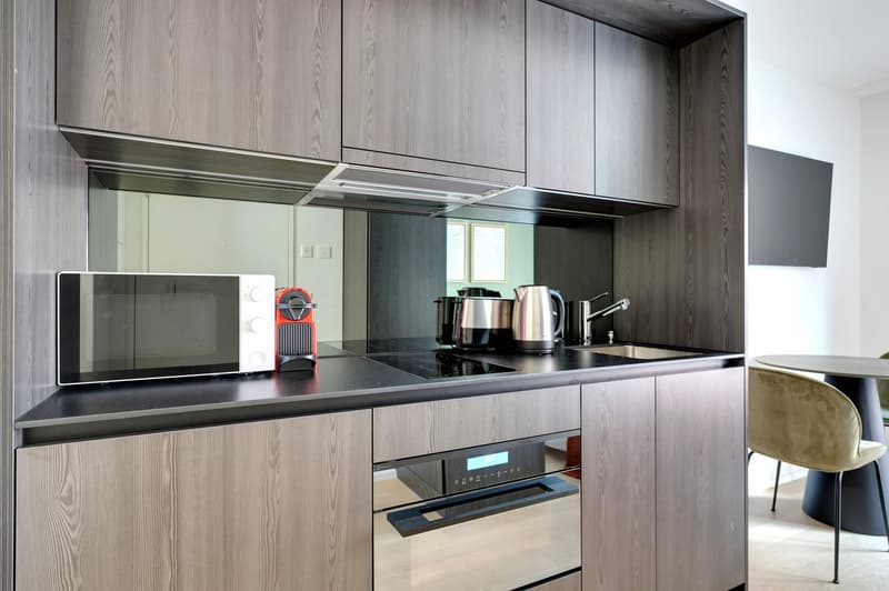 Modern kitchen with gray wood-paneled cabinets, black countertop, built-in microwave, coffee maker, and electric kettle