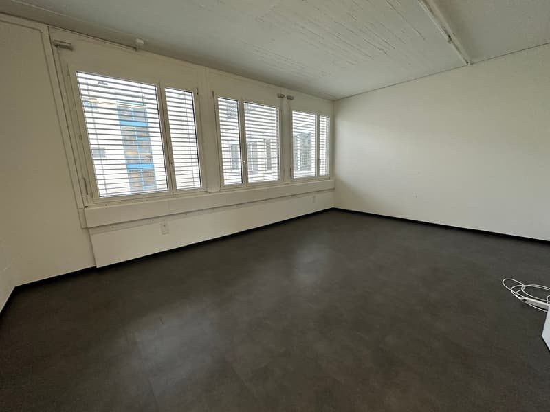 empty room with large windows, black floor, white walls, electrical outlet