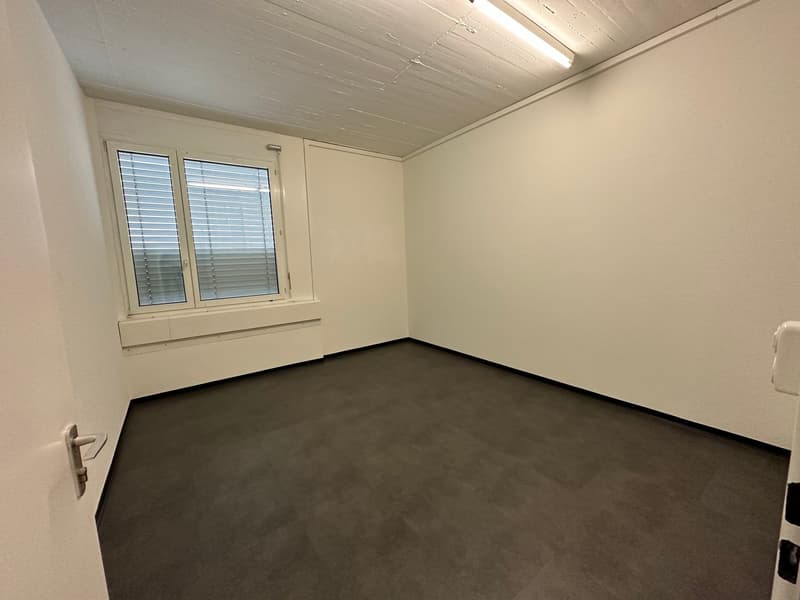 empty room with window, white walls, wooden ceiling, gray flooring