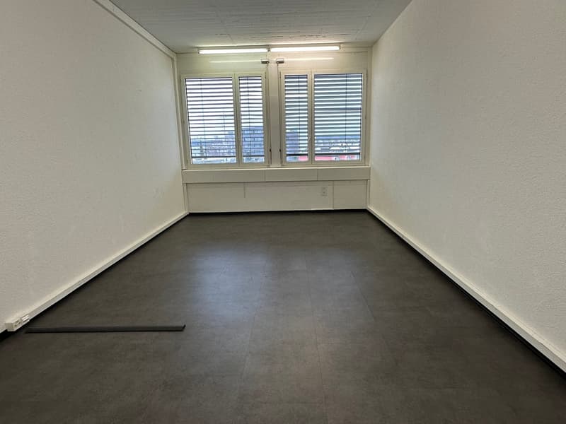 empty room with white walls, black flooring, and a window with shutters