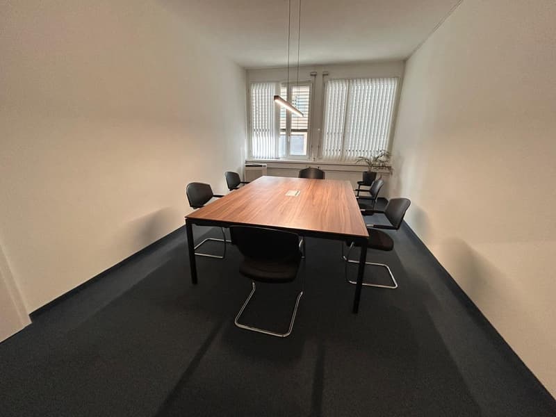 modern meeting room, rectangular wooden table, black chairs, white walls, two windows with blinds, pendant light