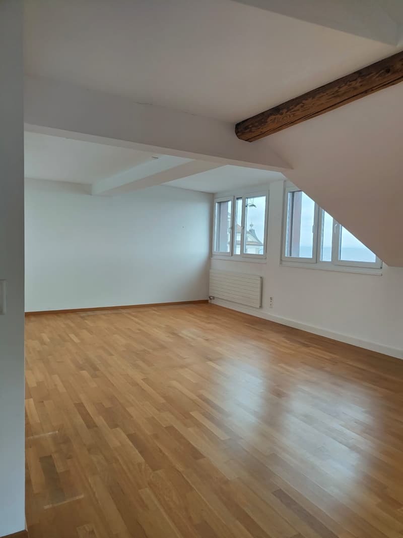 empty room, wooden floor, white walls, two windows with ocean view, white radiator, power outlet, exposed wooden beam