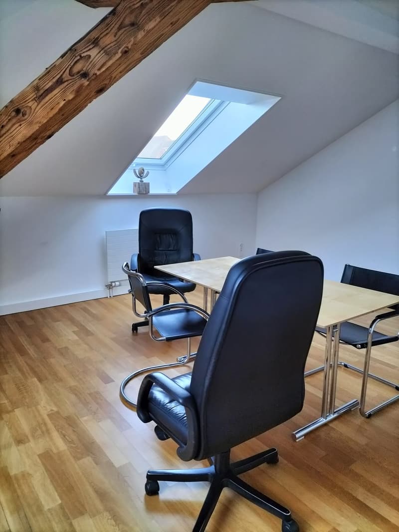 Attic office space with wooden beams, skylight, leather office chairs, and a wooden table