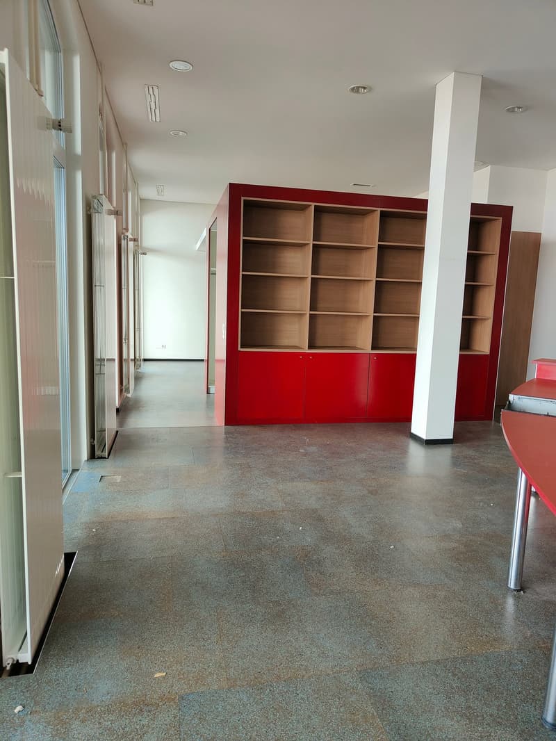 empty office room, red cupboard with shelves, white ceiling, gray floor, windows with sliding doors, red table