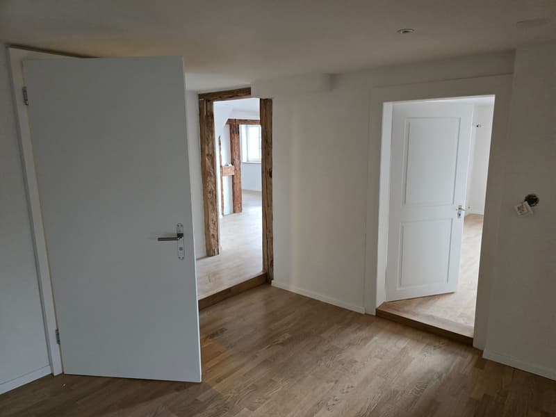 empty room, wooden floors, white walls, two open doors, another room visible