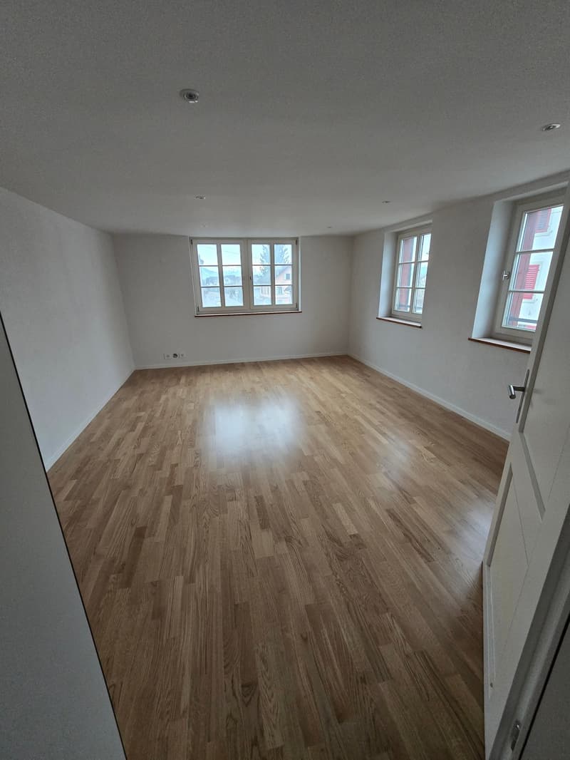 large room, hardwood floors, 3 windows, white walls, bright, no furniture