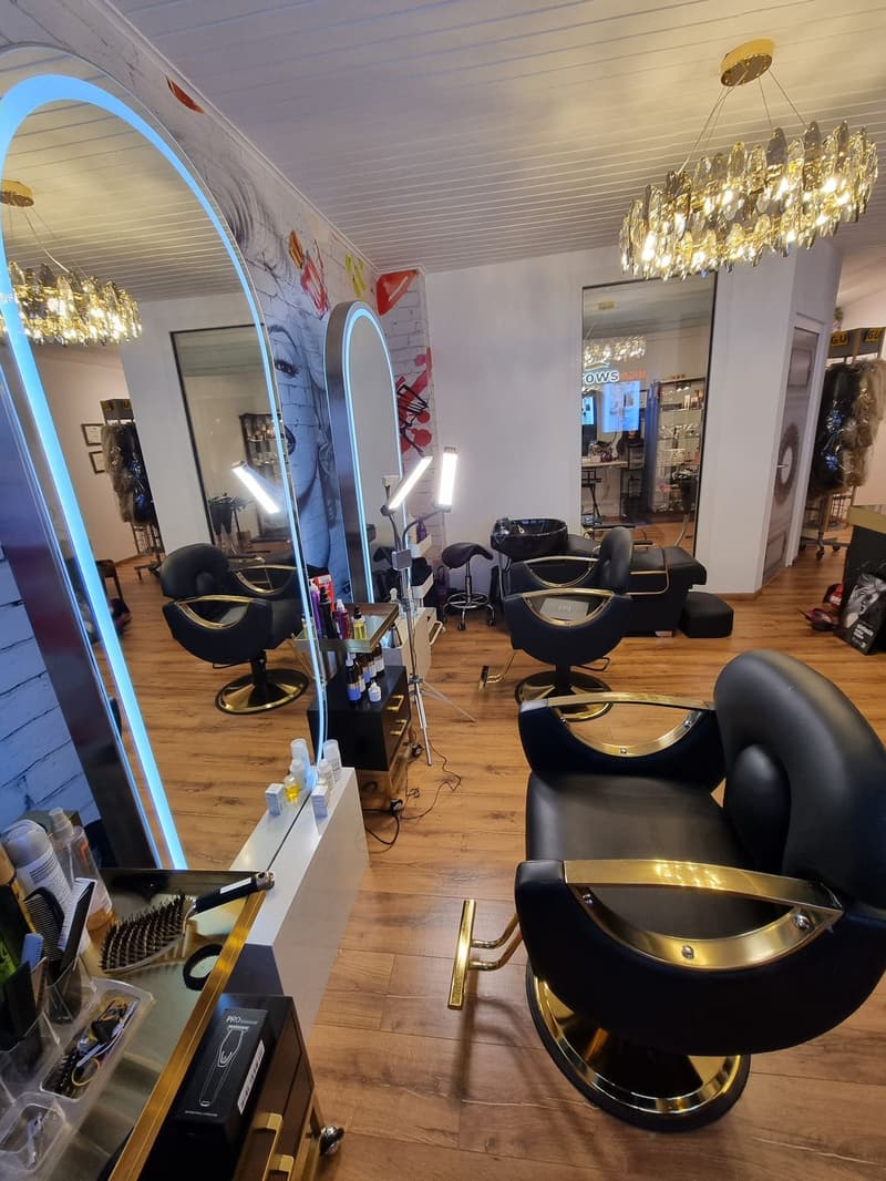Interior salon room with black high chairs, wooden floor, mirrors, cabinets, lamps, wall with picture.