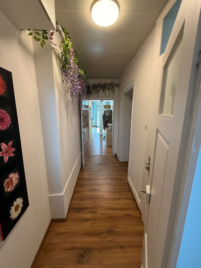 hallway with wooden floors, white walls, ceiling light, wall decor with flower paintings, doors on both sides