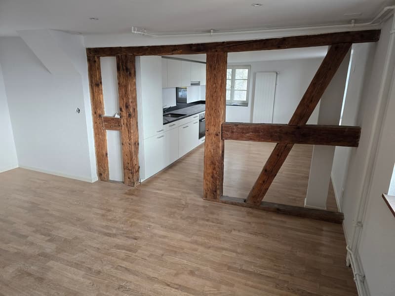 open floor plan with hardwood floors, wooden beams, white kitchen cabinets, a sink, and a window