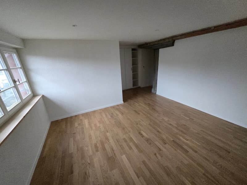 Empty room with hardwood floors, white walls, large window, wooden beam in the ceiling