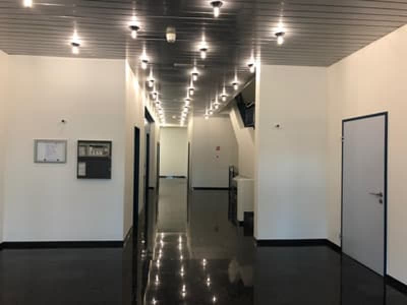 White walls, black floor, lights on the ceiling, doorways, picture frame on the left wall, equipment on the right wall