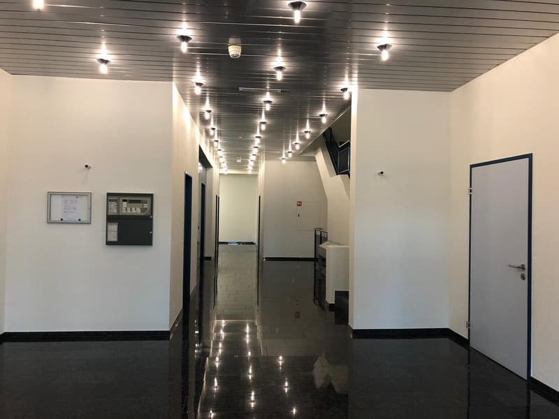 empty corridor with white walls, ceiling lighting, tiled floor, closed doors