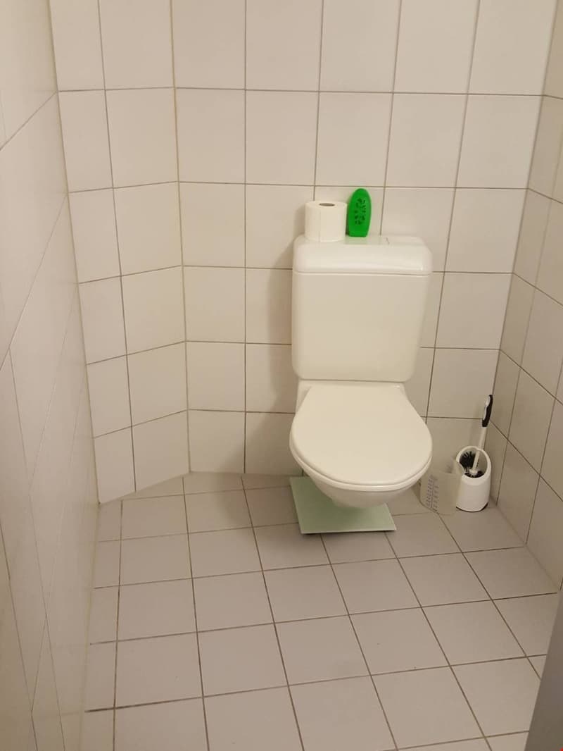 White toilet, white tiles on the walls and floor, a white toilet paper dispenser, and a white washing machine.