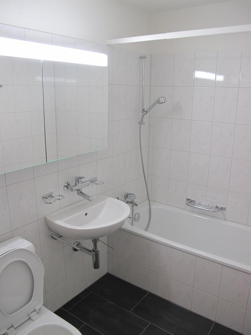 Bathroom with white tiles, white bathtub, white sink, silver faucet, silver shower head, white toilet, mirror